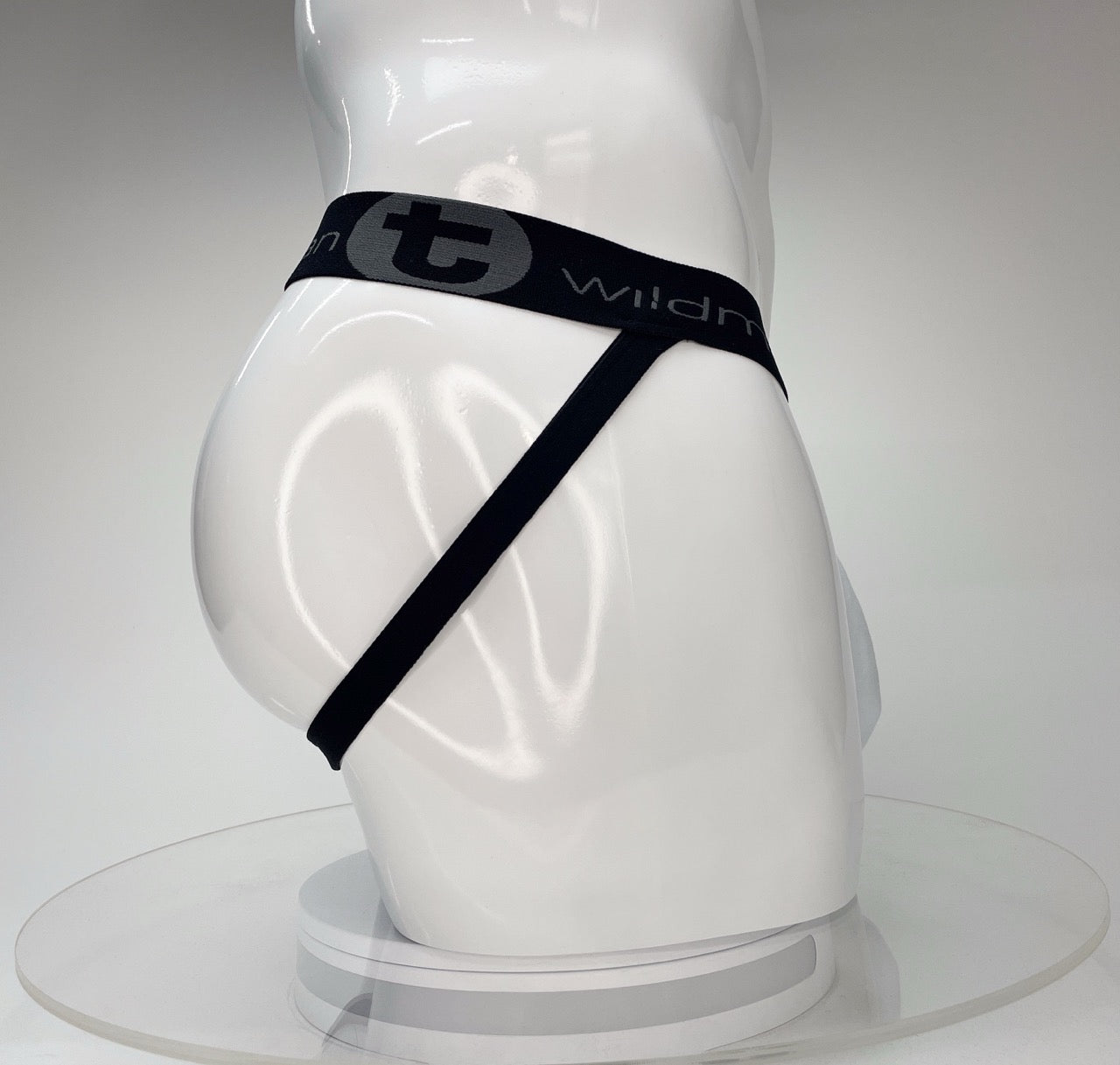 White WildmanT Big Boy jockstrap featuring a black waistband with gray logo text and branding on a white mannequin.
