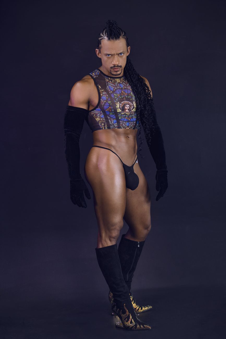 A man wearing a candyMan 99805 stained glass black print sheer patterned crop top with gold and blue designs