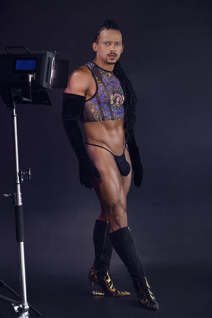 A man wearing a candyMan 99805 stained glass tank top in black with gold patterns and matching thigh-high boots