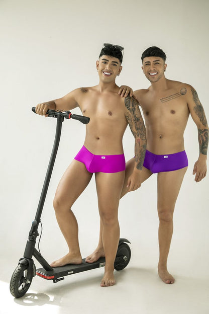 Two men wearing fitted magenta and purple CandyMan trunks with a sleek, minimalist cut.