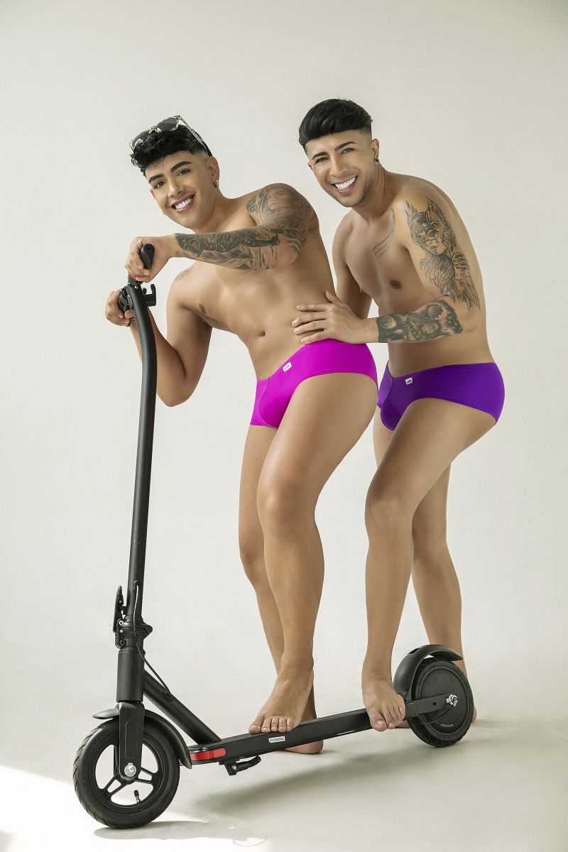 Two men wear magenta CandyMan 99943 trunks with a smooth, fitted cut, while standing together on a black scooter.