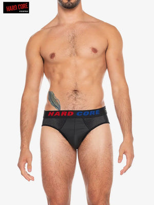 Men's black backless brief with mesh panels and a colorful waistband worn by a model by Hard Core