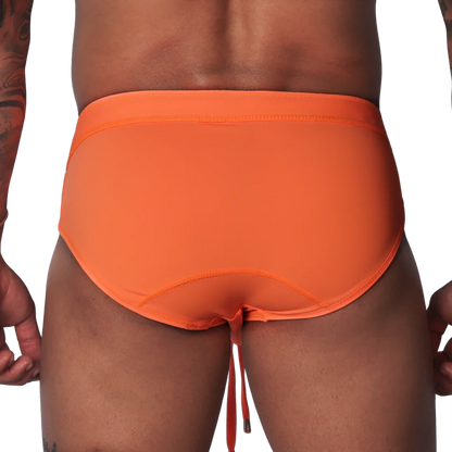 Bright orange swim brief with a wide waistband, contoured back seams, and dangling drawstring against black background.
