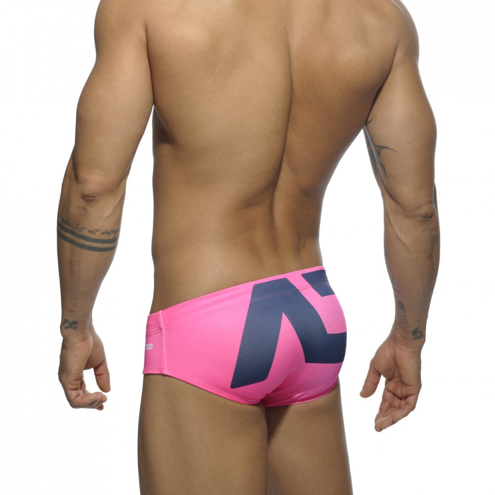 Bright pink extra-large logo brief swim trunks showing the back with a bold navy blue geometric logo