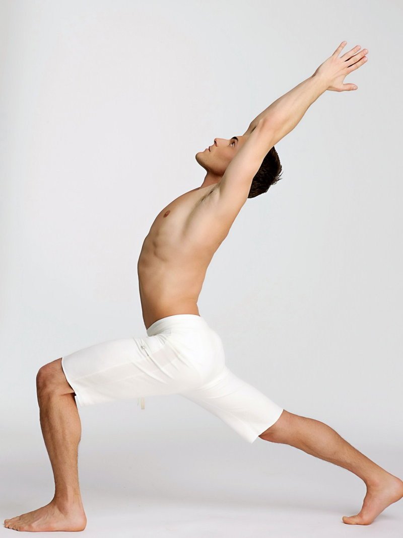 A man in white eco-track short yoga shorts performing a dynamic stretching pose showing the front view