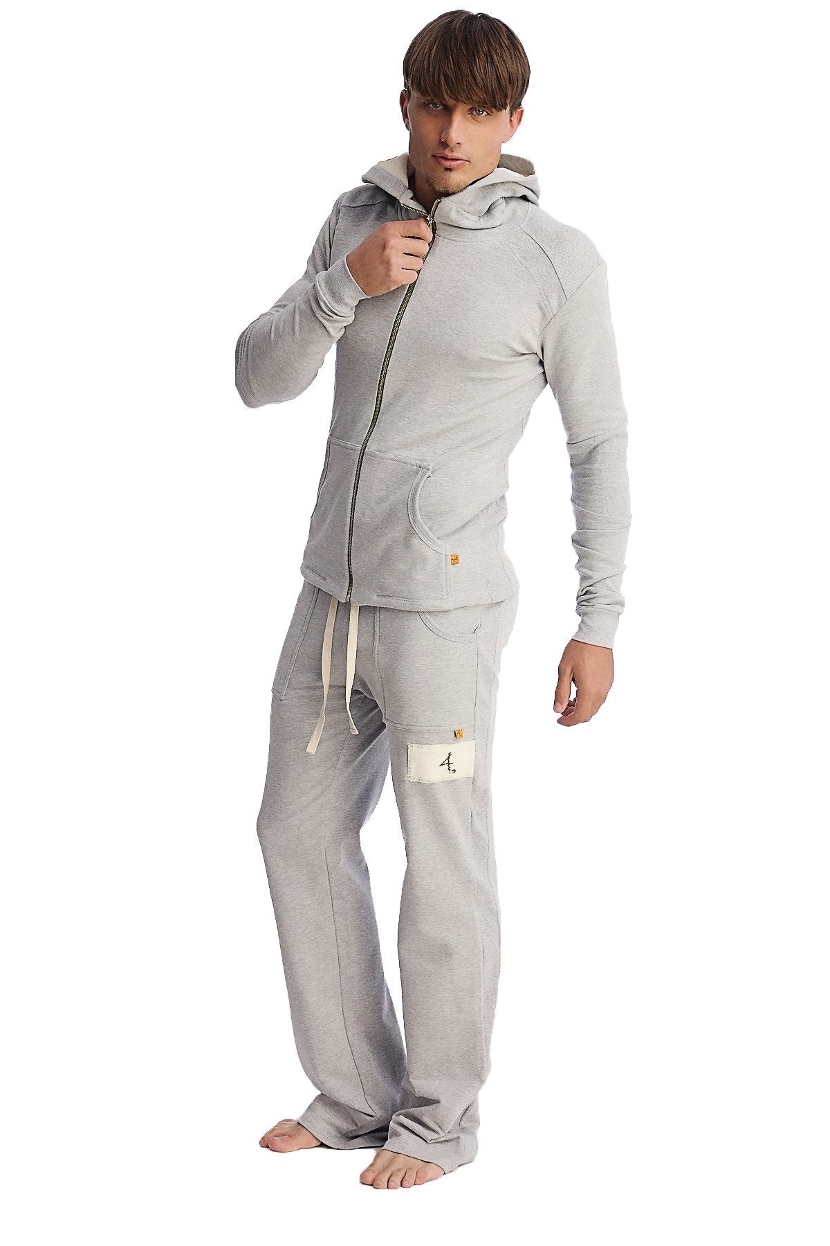 A man wearing heather grey edge eco-track and yoga sweatpants with side pockets and a matching light gray zip hoodie