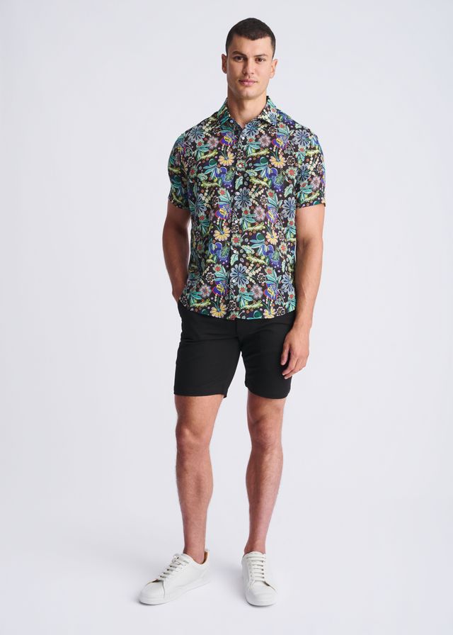 A man wearing a floral lightweight linen tencel short-sleeved shirt with multicolored pattern on a dark background