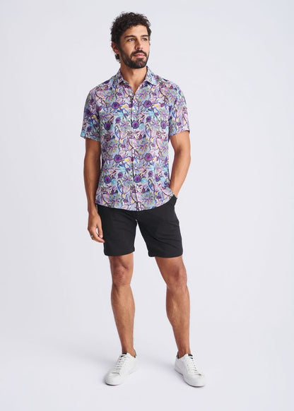 A man wearing a floral lightweight linen tencel short-sleeved shirt in shades of purple blue and pink