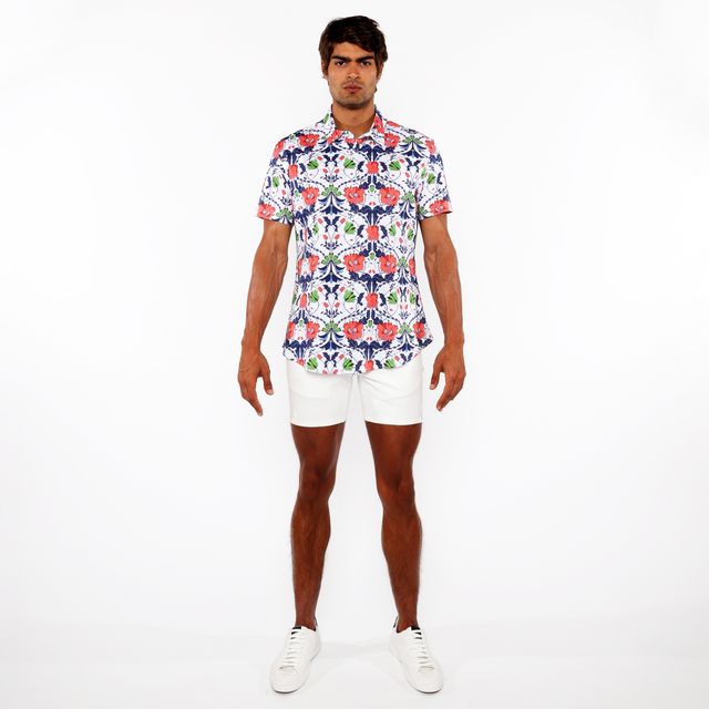 A man wearing a floral print stretch knit shirt with red blue and green flowers on white short-sleeved button-up shirt