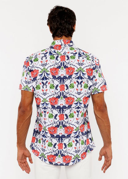A man wearing a white floral print stretch knit shirt with red poppies and green leaves on navy blue vines