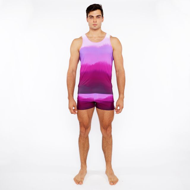 A man wearing a gradient printed swim short and matching tie-dye tank top in purple and pink colors