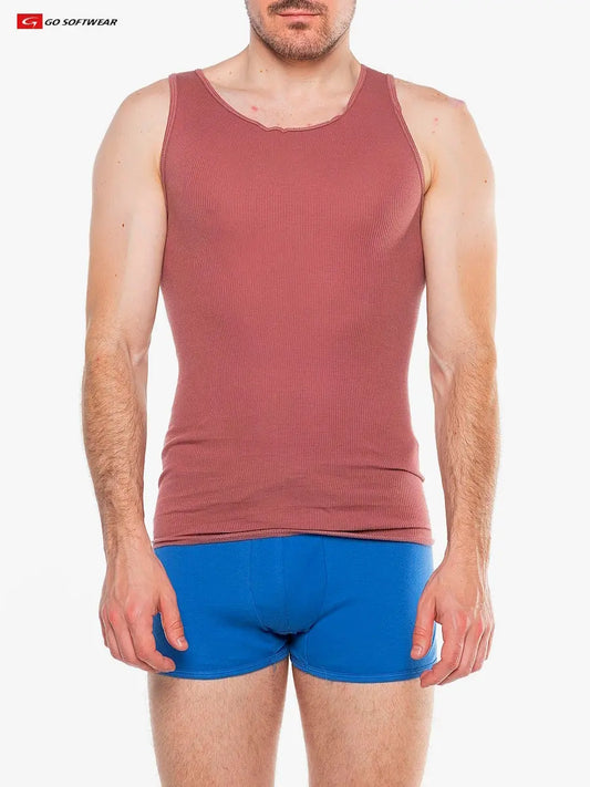 A man wearing a red clay ribbed tank top by Go Softwear paired with blue boxer shorts standing against a plain white background