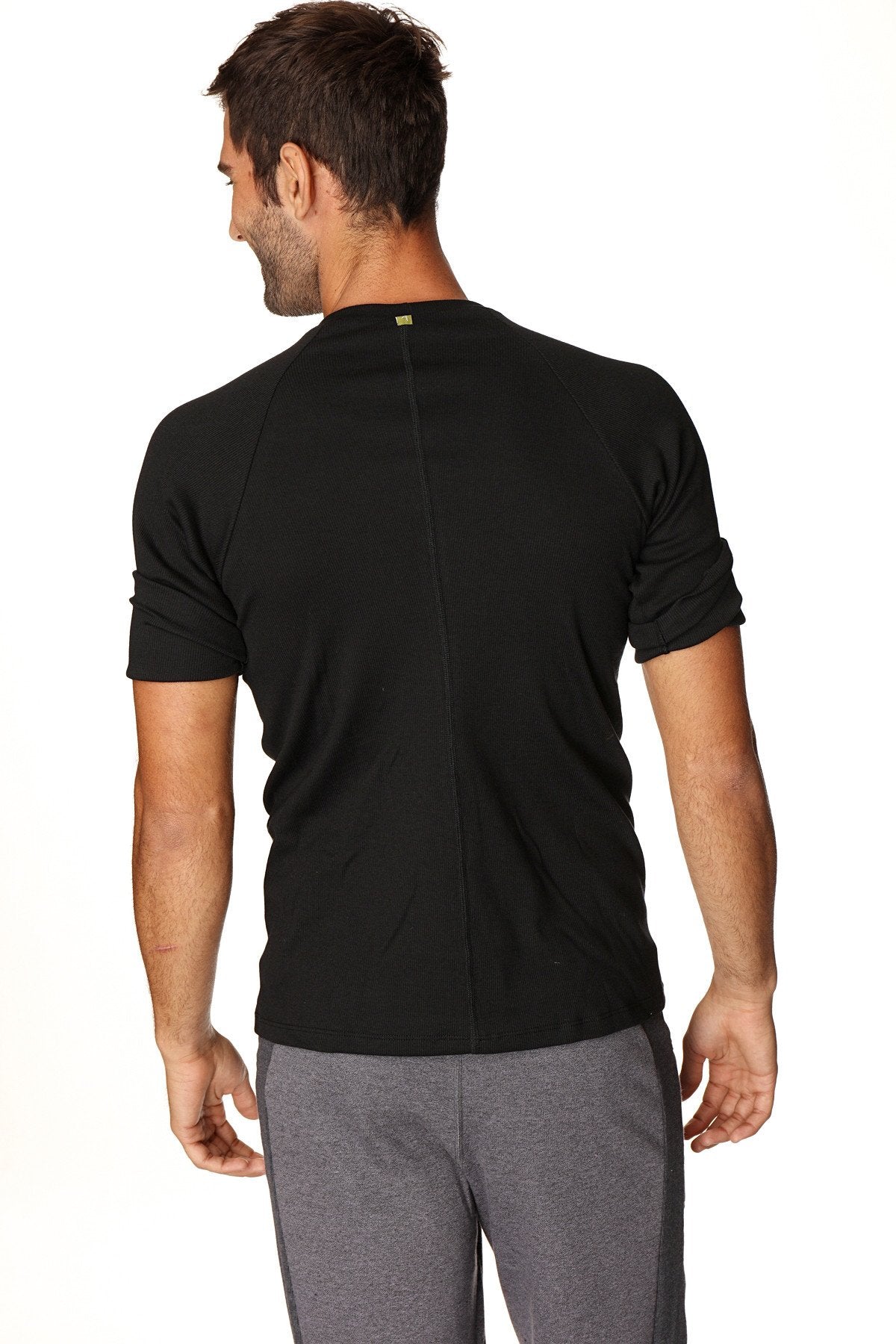 Back view of hybrid crew neck raglan tee black short-sleeved athletic shirt with subtle vertical seam and green logo