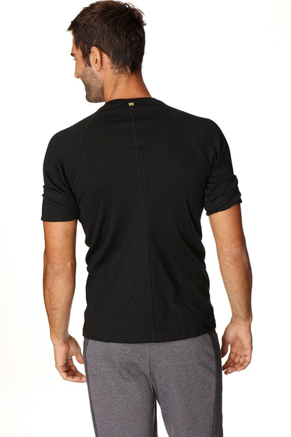 Back view of hybrid crew neck raglan tee black short-sleeved athletic shirt with subtle vertical seam and green logo
