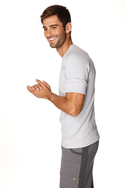 A man wearing a heather grey hybrid crew neck raglan tee with subtle texture and dark grey athletic pants with side stripes