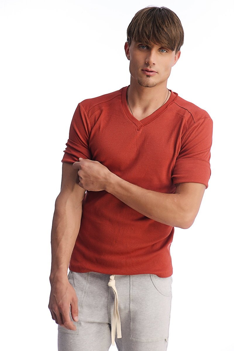 A man wearing a rust-colored hybrid v-neck short-sleeved shirt with ribbed cuffs and hem in cinnabar color
