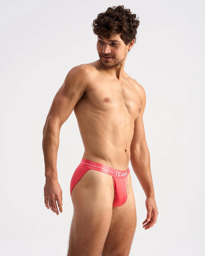 Bright coral-red icon sports brief with white elastic waistband featuring team logo in form-fitting design