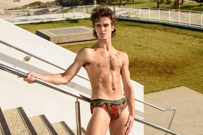 Men's swim briefs in red with rose print made by Maris Equi shown on a model outdoors.