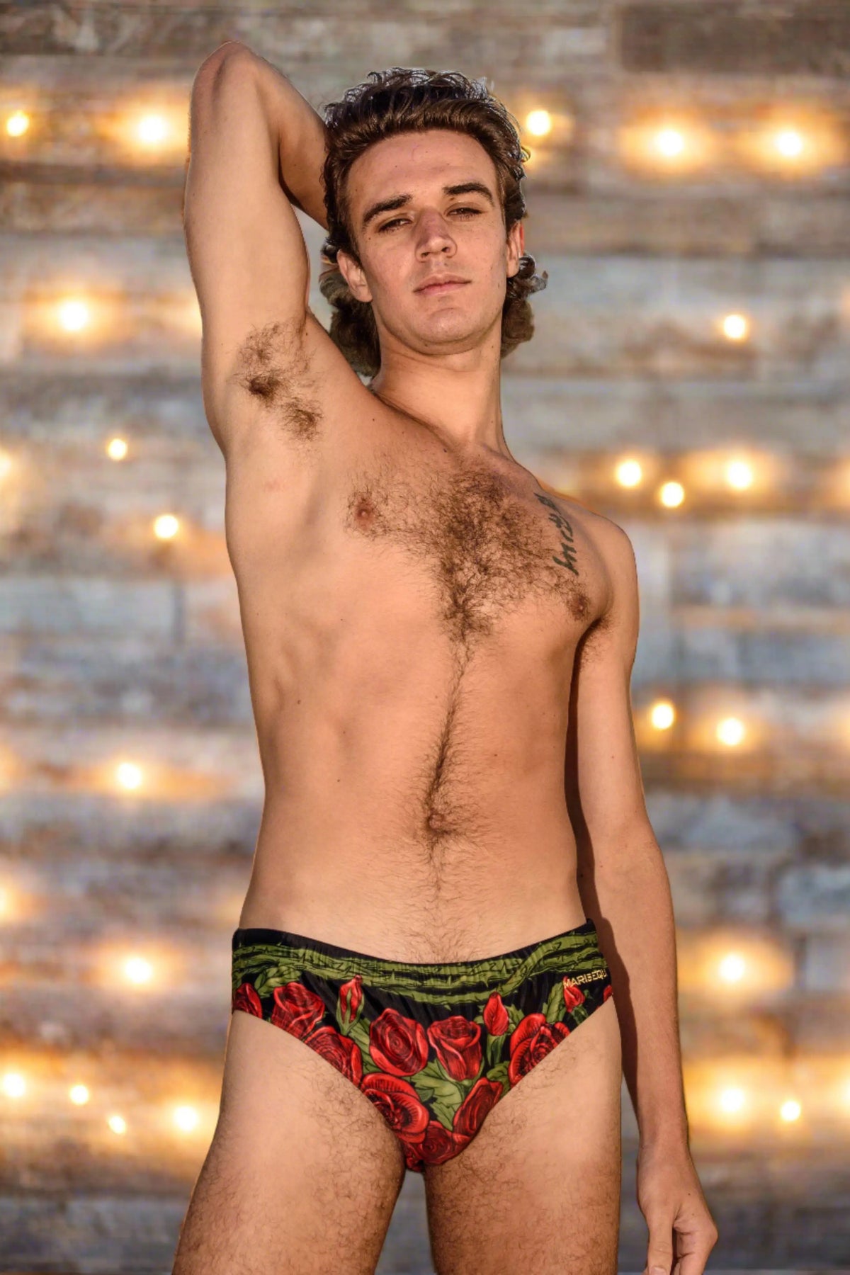 Men's swim briefs in black with red rose print featuring a comfortable waistband shown by a model by Maris Equi