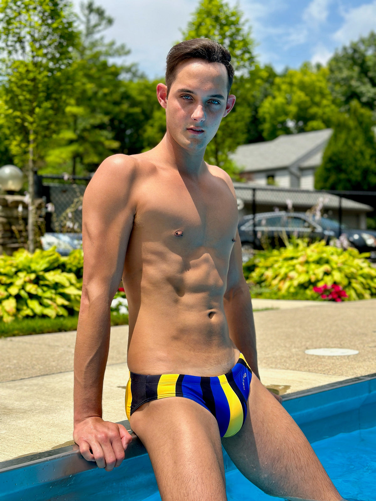 Men's swim briefs in blue and yellow stripes made by Maris Equi shown on a model by a poolside.