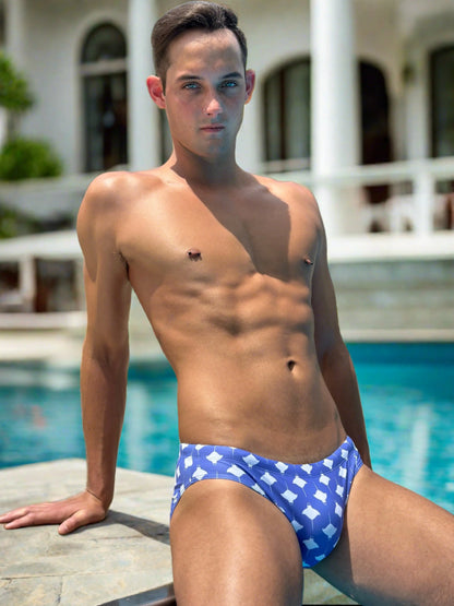 Men's swim briefs in blue with white manta ray pattern made by Maris Equi shown on a model by a pool.