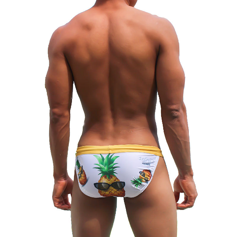 White swim trunks with yellow waistband and playful pineapple graphic wearing sunglasses from icker sea swimwear