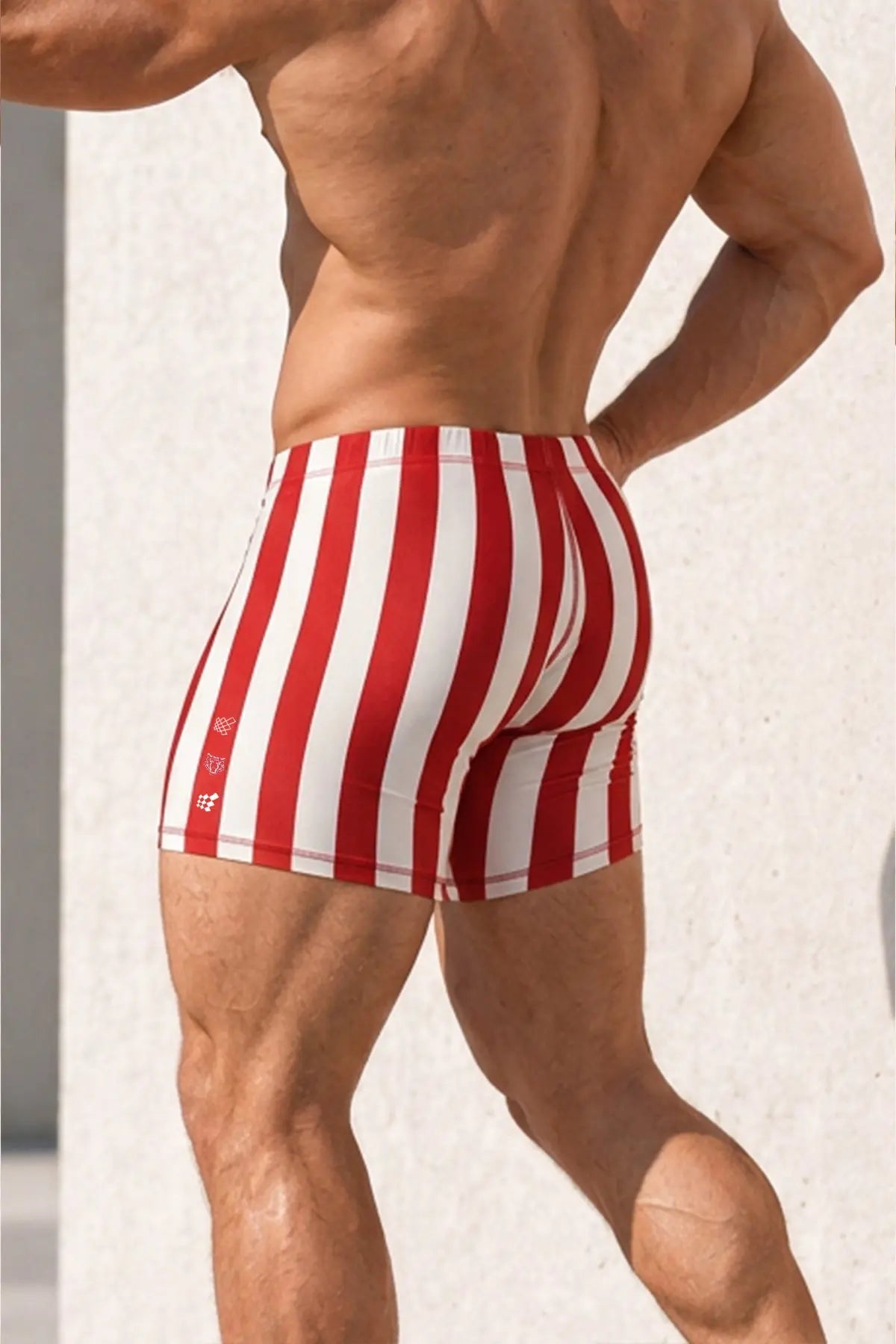 Red and white striped bodybuilding shorts worn by a muscular male model showcasing a fitted design and elastic waistband by Jed North