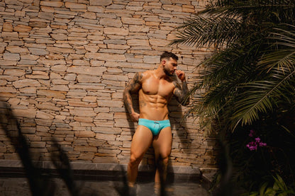 A muscular man wearing jor 2387 travel swim briefs in bright turquoise with a drawstring waistband