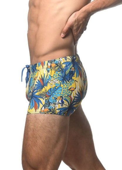 Vibrant yellow jungle printed swim trunk with tropical blue green and orange toucans and palm leaves pattern