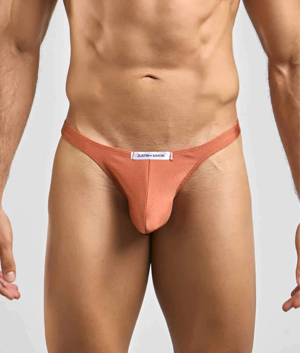 A sleek peach-colored justin simon classic tanga thong made of smooth form-fitting fabric with a minimalist design