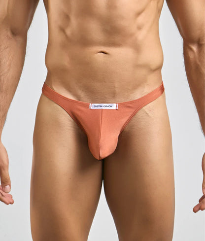 A sleek peach-colored justin simon classic tanga thong made of smooth form-fitting fabric with a minimalist design
