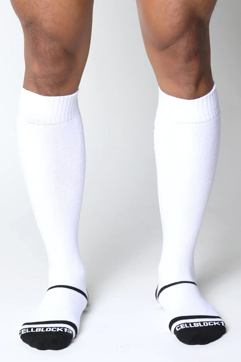 White knee-high socks with black trim and ribbed texture featuring cellblock 13 branding on the heel back view