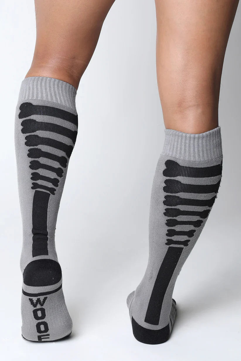 Gray kennel club bones knee high socks with black skeletal design and wood printed on the heel visible from the back