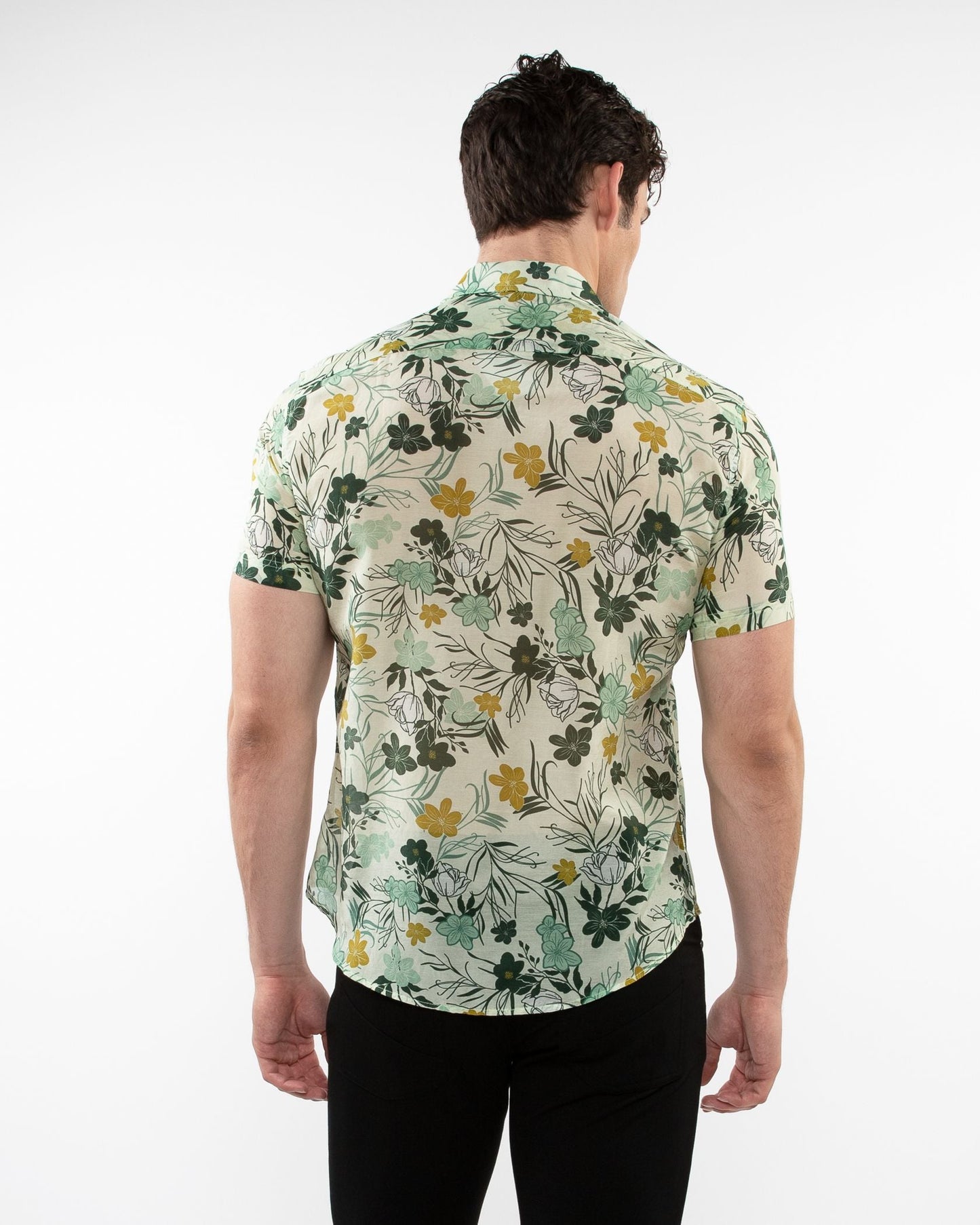 A man wearing a lightweight cotton silk short-sleeved shirt with green yellow and black floral pattern on off-white background
