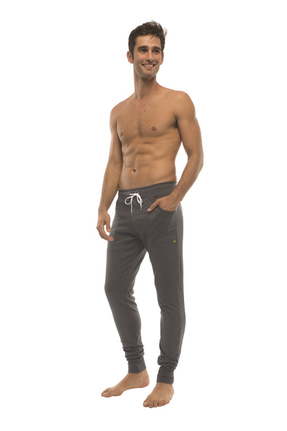 Long cuffed jogger and yoga sweat pants in charcoal with white drawstrings and a gold logo on the left thigh
