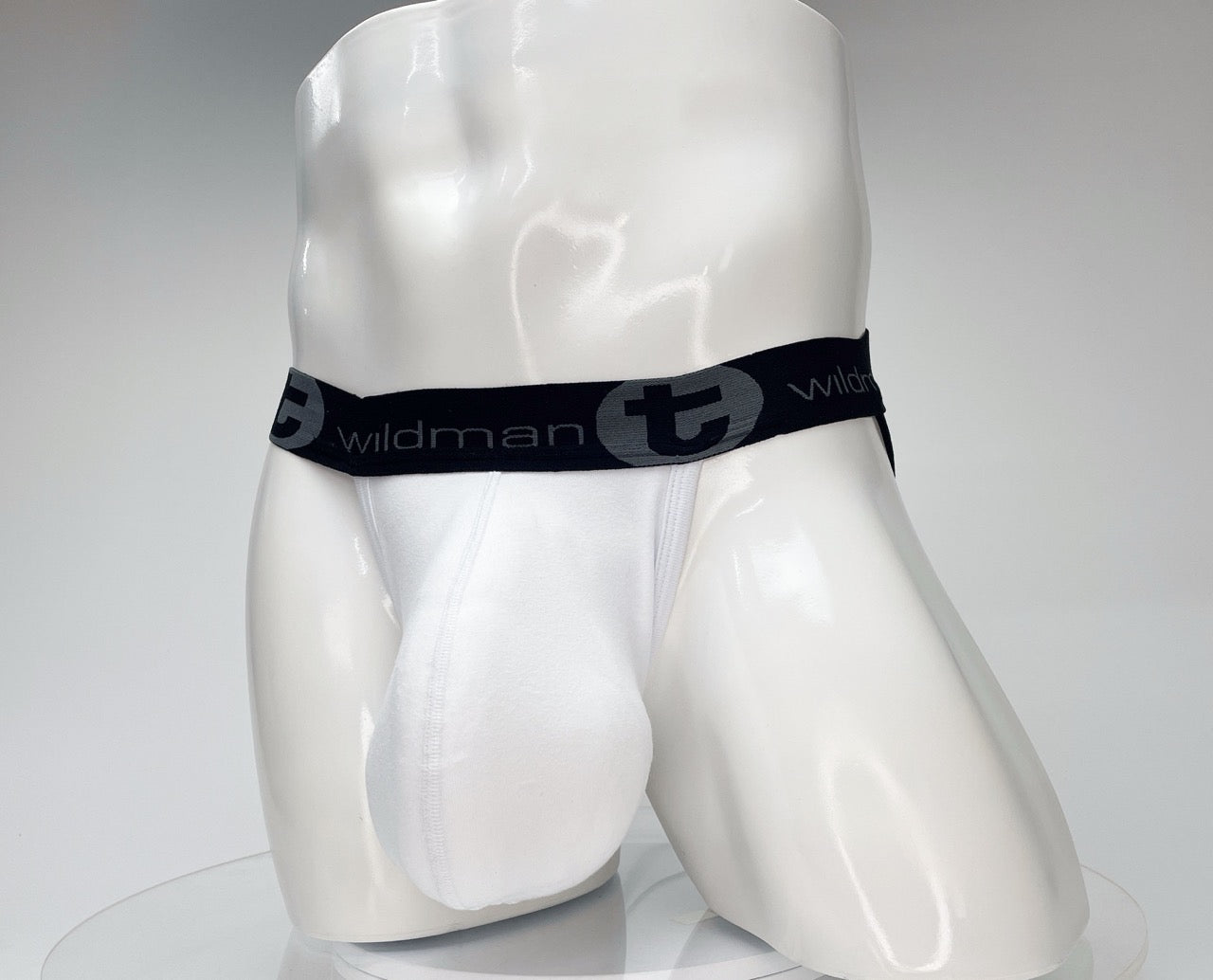 White jockstrap with a contoured pouch on a white mannequin, featuring a black waistband with "wildmanT" branding.