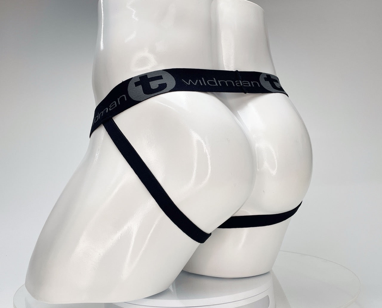 White jockstrap on a mannequin, featuring a black waistband with "WildmanT" branding and thin black leg straps.