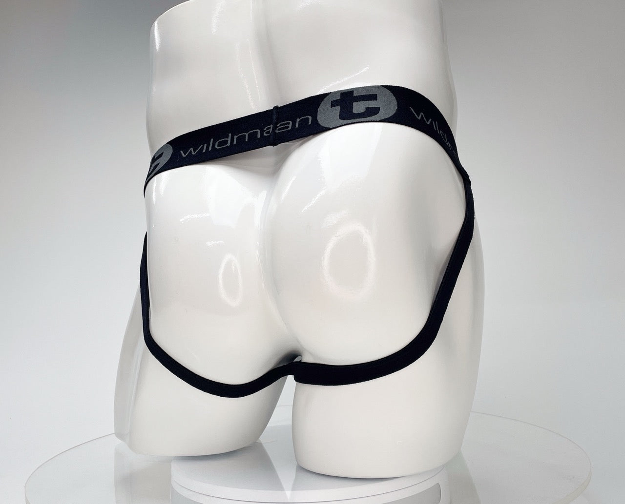 White jockstrap on a mannequin, featuring a black waistband with WildmanT logo and thin black leg straps.