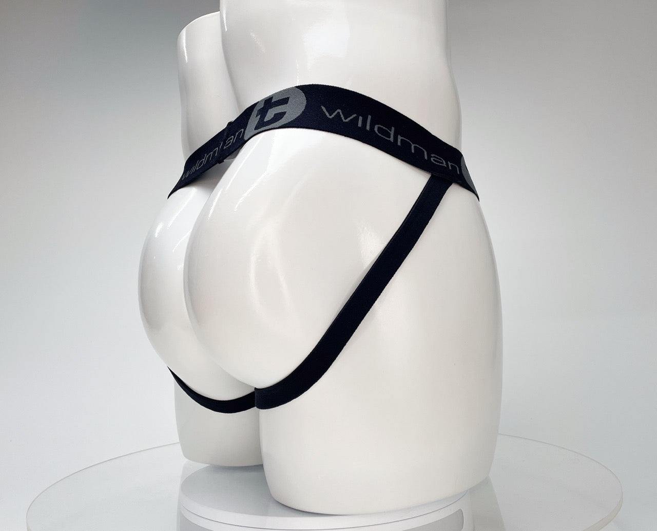 White WildmanT jockstrap on a mannequin, featuring a black branded elastic waistband and side straps.