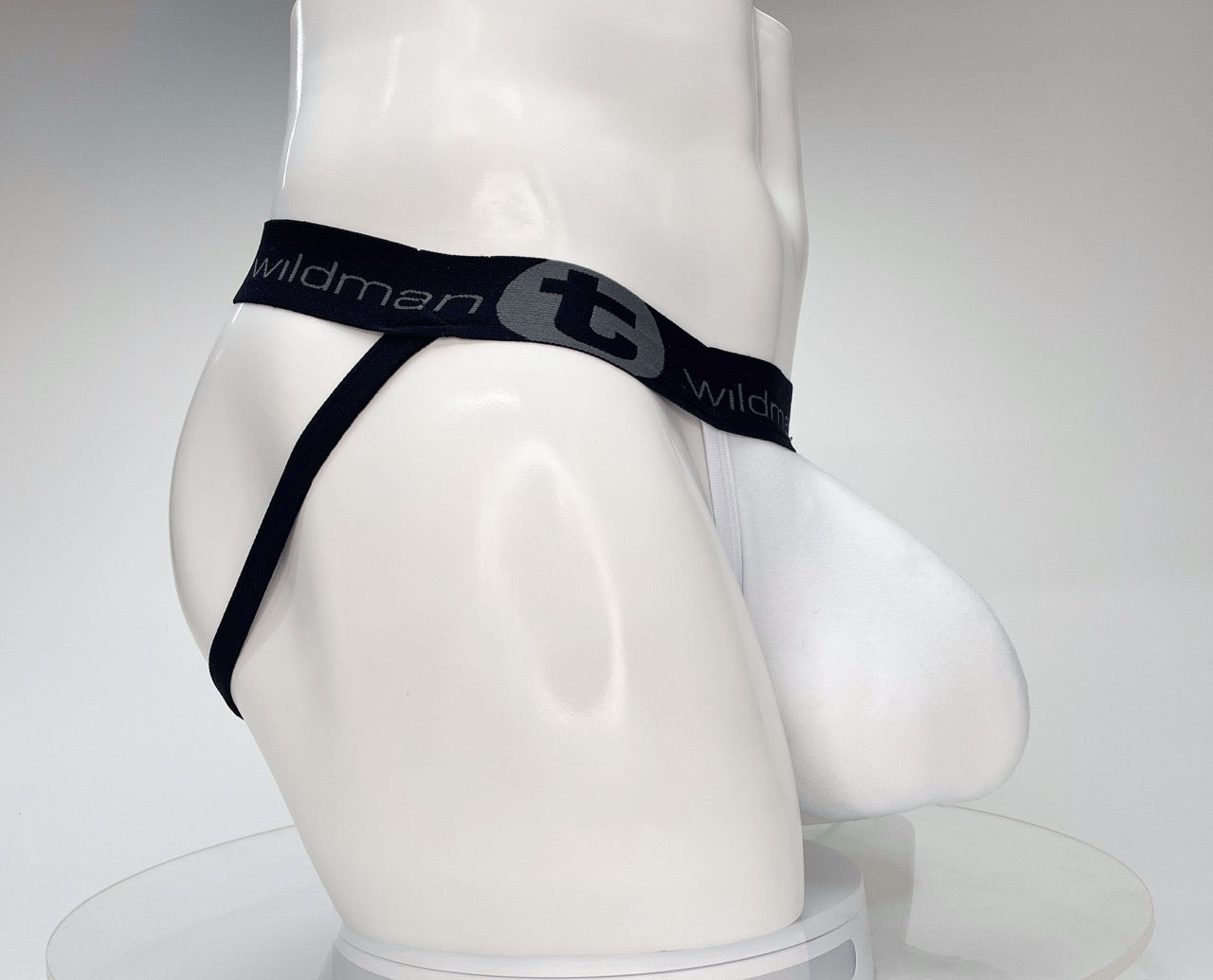White jockstrap on a mannequin with a large pouch and a black branded waistband featuring the WildmanT logo.