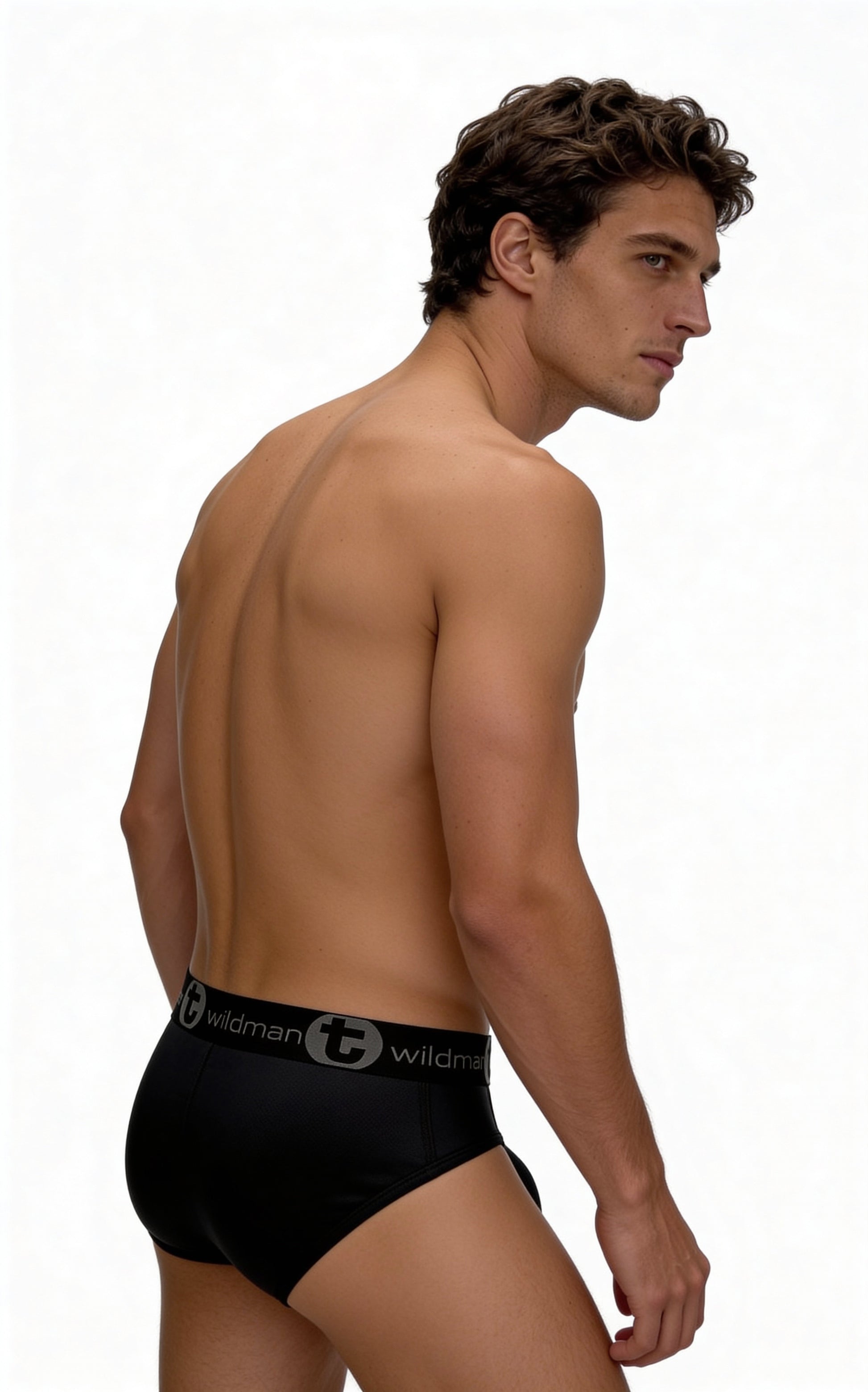 A model wears WildmanT black mesh brief underwear with a branded logo waistband, shown from a side-profile angle.