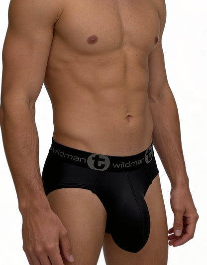 A muscular model wearing black WildmanT mesh briefs with a prominent contoured pouch and logo waistband.