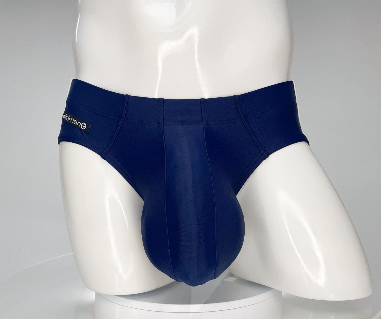 Navy blue WildmanT swim brief on a white mannequin with a prominent, contoured front pouch and side logo tag.