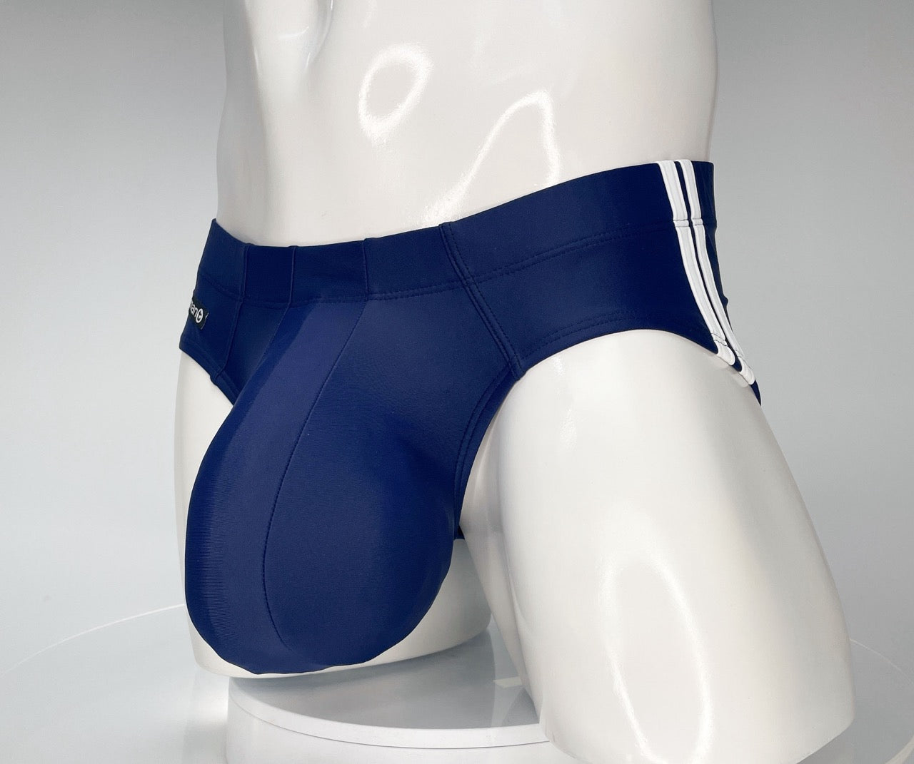 Navy blue swim brief with a large, contoured pouch and white side-stripe detailing on a mannequin torso.