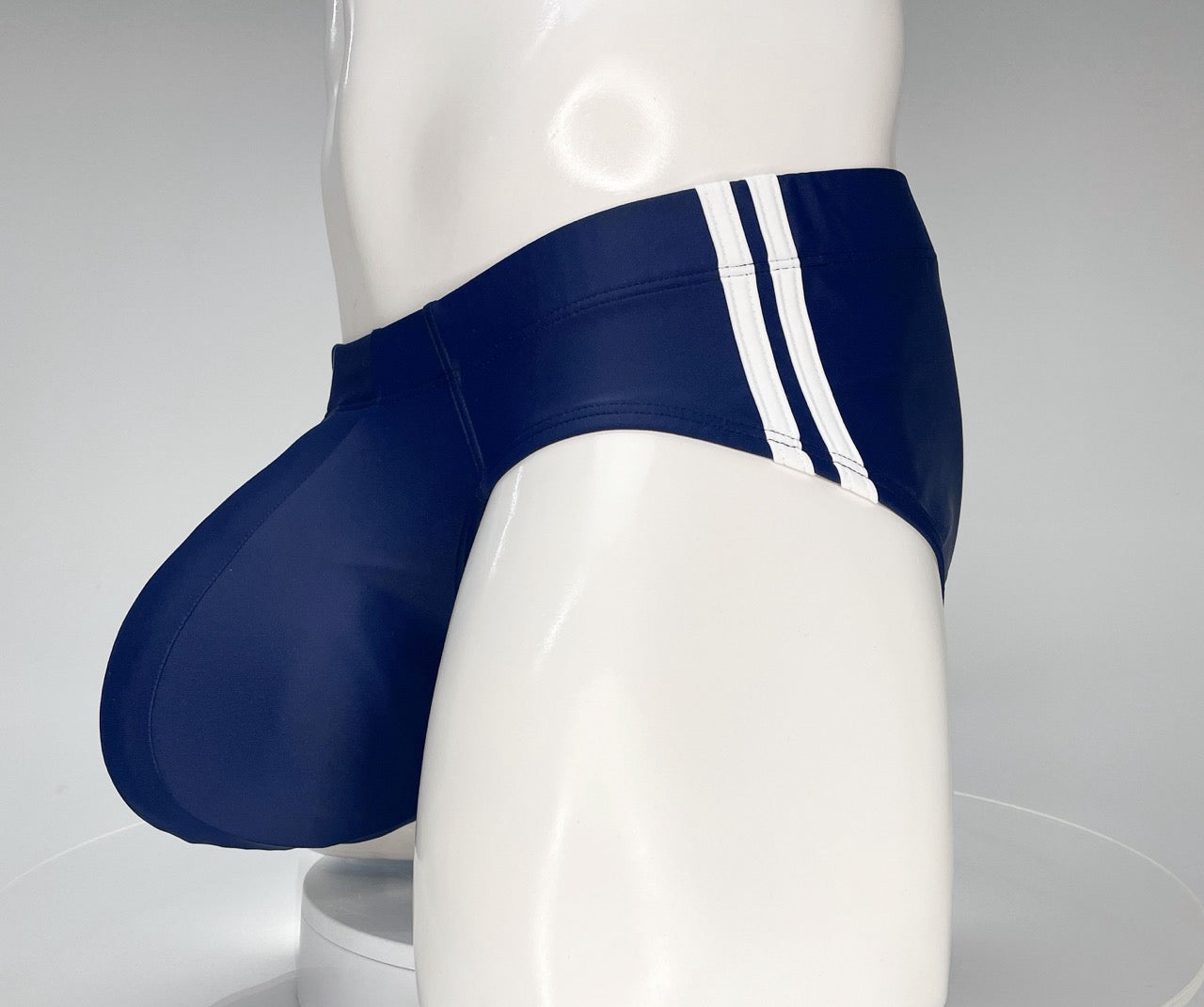 Navy blue swim brief with a large, contoured pouch and dual white side stripes on a white mannequin torso.