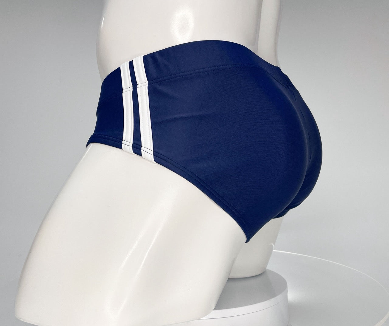 Navy blue swim brief with two vertical white side stripes on a white mannequin.
