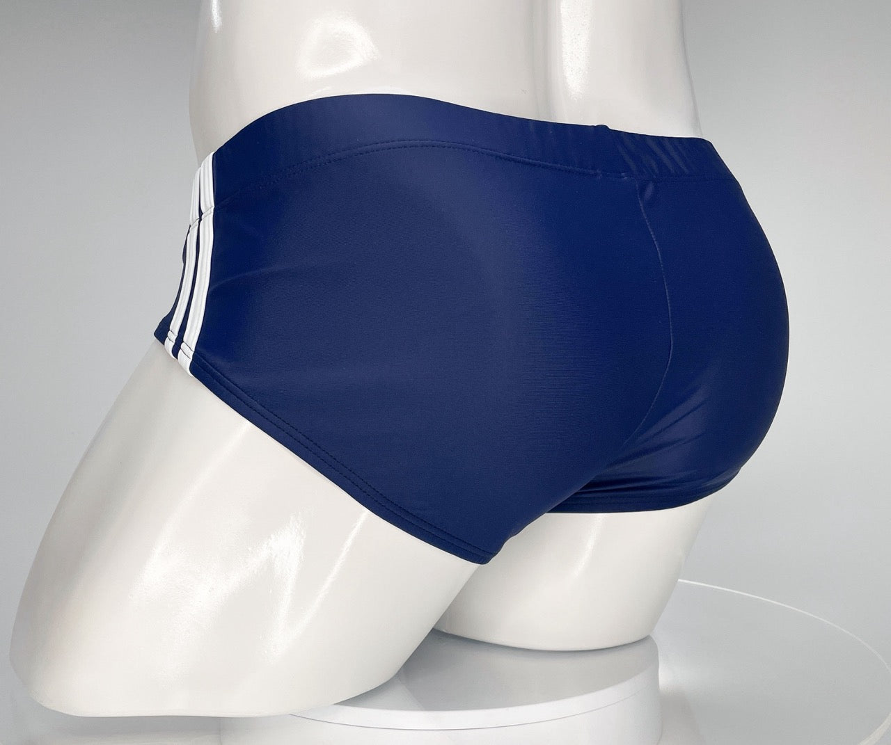 Navy blue swim brief on a mannequin, featuring two white side stripes and a fitted, low-cut athletic style.
