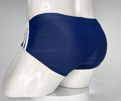 Navy blue swim brief on a mannequin, featuring two white side stripes and a fitted, low-cut athletic style.