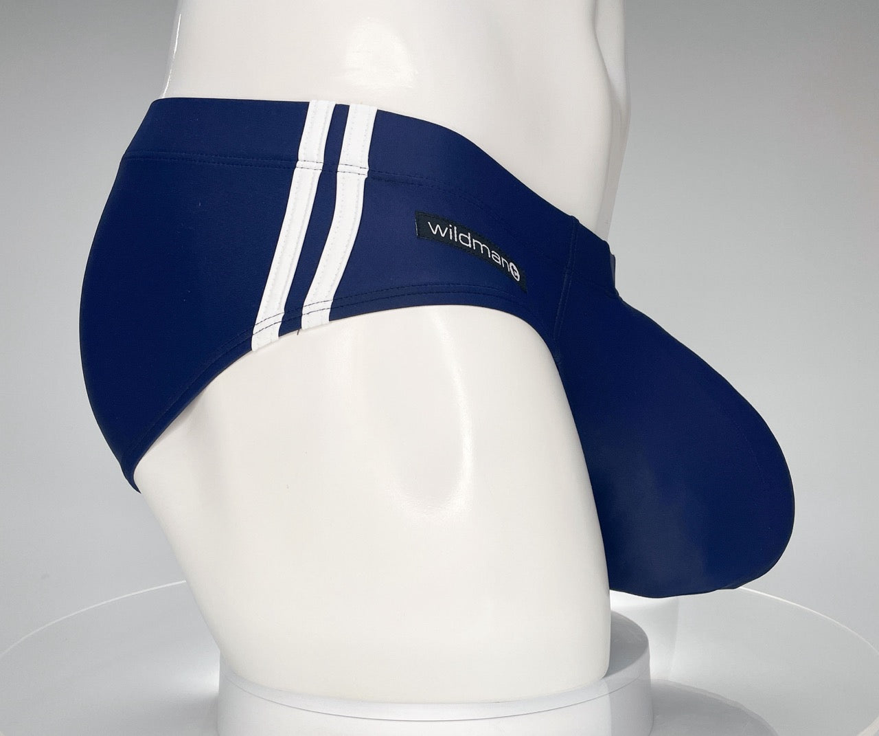 Navy blue WildmanT swim brief with white side stripes and a branded tag, shown from a side profile on a mannequin.