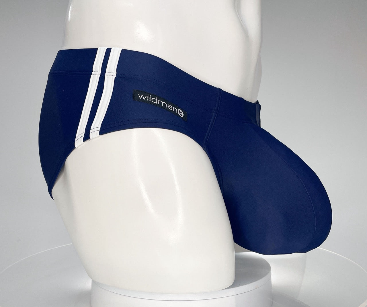 Navy blue WildmanT swim brief with white side stripes and a prominent contoured pouch on a white mannequin torso.